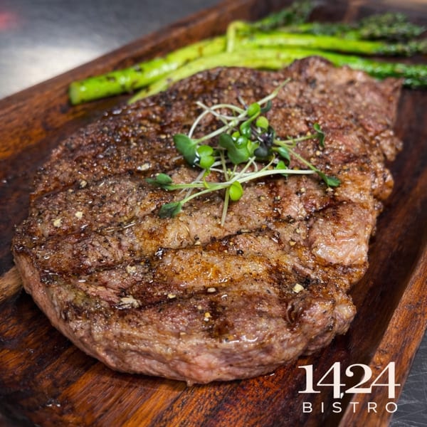 Grilled steak with microgreens and asparagus on a wooden board at 1424 Bistro.