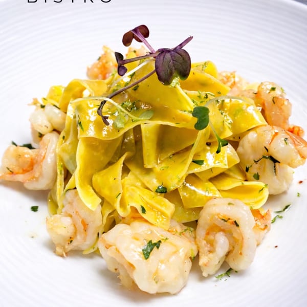 Close-up of pappardelle pasta with shrimp and fresh herbs on a white plate.