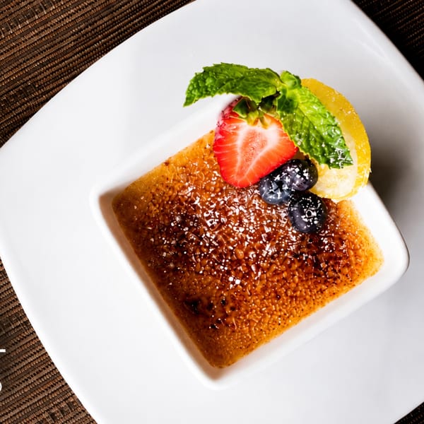 Crème brûlée with fresh strawberries, blueberries, mint, and a lemon slice on a white plate.