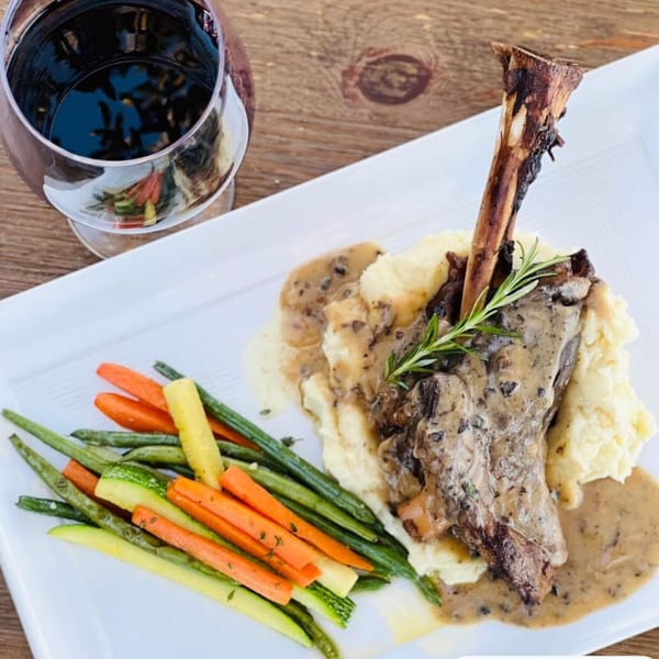 European lamb shank with mashed potatoes, gravy, roasted vegetables, and a glass of red wine.
