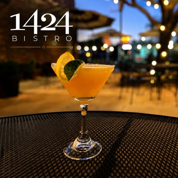 A vibrant orange cocktail garnished with lemon and lime on a bistro table at dusk.