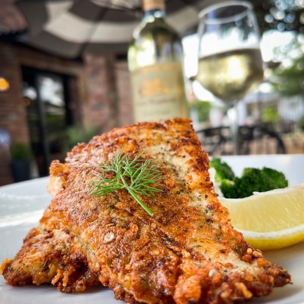 Crispy fried fish with dill, lemon, and broccoli, paired with white wine on a patio.
