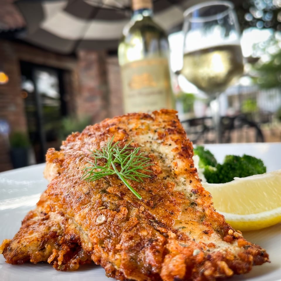 Crispy fried fish with dill, lemon, and broccoli, paired with white wine on a patio.