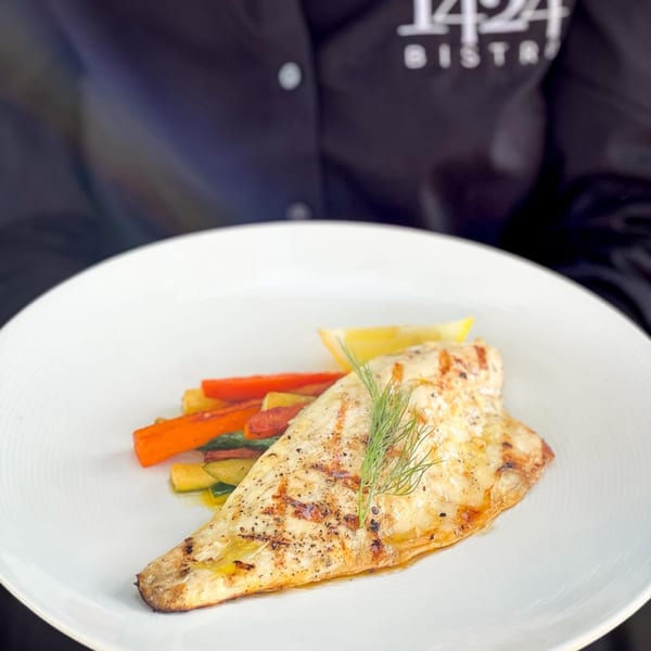 Grilled fish fillet with roasted vegetables and a lemon wedge on a white plate at 1424 Bistro.