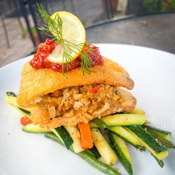 Fried fish fillet stuffed with crab meat, topped with red sauce, lemon, and dill, served with vegetables.